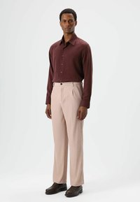 Bordeauxrode longsleeve blouse met knopen, gecombineerd met lichtroze geplooide broek en donkerbruine schoenen. Gladde stof met duidelijke texturen.