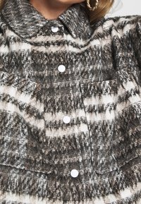 Overhemd met knopen in een gestructureerde stof met een zwart-wit-bruin ruitpatroon, met een kraag en twee voorzakken.