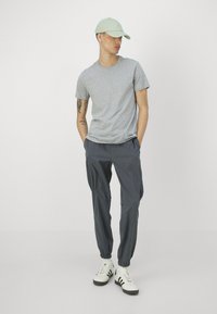 Grå kortermet t-skjorte, grå smal joggebukser med elastiske cuff, hvite sneakers med svarte striper, og en lys grønn caps.