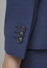 Granatowa dopasowana marynarka z teksturowanym materiałem, z rękawami wyposażonymi w trzy czarne guziki z czterema otworami każdy oraz subtelnymi detalami w ściegach.