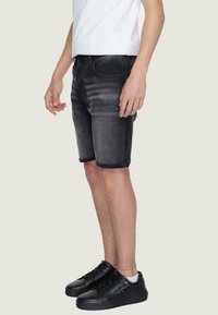 Pantaloni shorts in denim nero con un leggero sbiadimento, orli arrotolati e design a cinque tasche, abbinati a sneaker nere, su uno sfondo chiaro.