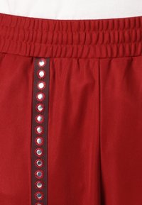 Röda tygshorts med elastisk midja har två vertikala linjer prydda med cirkulära paljetter och kontrasterande sömmar.