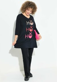 Musta tunikka, jossa on kimalteleva "HO" teksti vaaleanpunaisena ja beigeä, V-kaula-aukko ja kolmen neljänneksen hihat. Yhdistetty mustiin housuihin ja korkokenkiin.