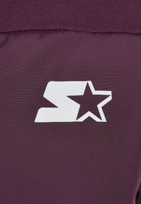 Lettre S stylisée blanche avec une découpe d’étoile sur le côté droit, imprimée sur un fond en tissu violet foncé.