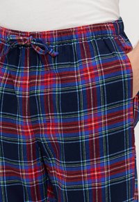 Tengerészkék kockás nadrág piros, kék és zöld mintával. Rugalmas derékpánttal, húzózsinórral és oldalzsebekkel rendelkezik. Pamut anyagú.