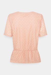 Top de color melocotón de manga corta hecho de encaje texturizado con un patrón en forma de chevron y un dobladillo peplum. La vista trasera muestra los detalles de las costuras.