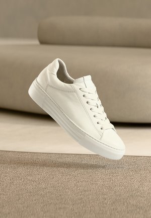 White leather sneaker featuring a classic design, with lace-up closure, flat rubber sole, and textured accents. Clean, minimalist aesthetic.