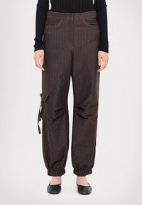 Pantalons marron à rayures avec une coupe décontractée, des poignets élastiqués, des poches avant et un détail latéral ajustable. Le tissu a une texture lisse.