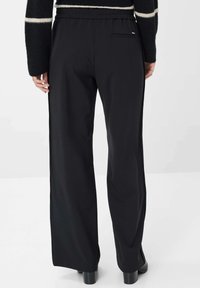 Pantalons larges noirs avec une taille plate, des poches latérales et une texture lisse. Dotés d'une poche arrière discrète et de détails minimaux.