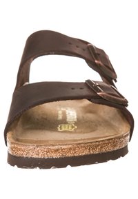 Sandalo in pelle marrone con due cinturini regolabili, soletta in sughero piatta e suola in gomma testurizzata. Design minimale con fibbie metalliche.