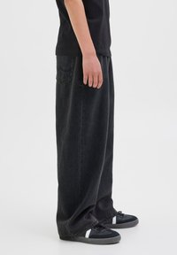 Crne široke traperice ravnog kroja, s džepom na stražnjoj strani i suptilnim izblijedjenjem. Uparen s crnim tenisicama s bijelim detaljima.