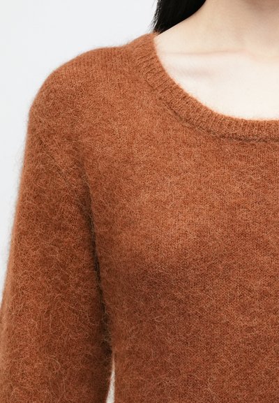 Gorčica oranžna jopica s krožnim ovratnikom, izdelana iz mehkega, puhastega materiala. Tekstura se zdi puhasto in lahkotno, z rebrastim detajlom na ovratniku.