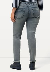Los jeans skinny grises presentan una cintura alta, dos bolsillos traseros y dobladillos deshilachados. Se llevan con botas negras de tobillo. Textura de denim suave.