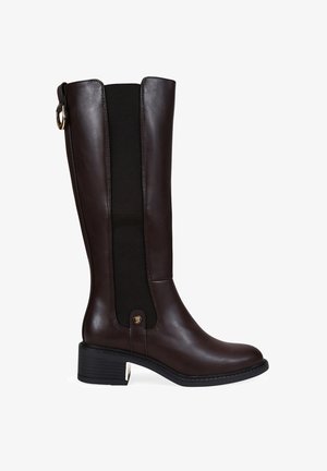 Bota de cuero marrón hasta la rodilla con panel elástico negro, puntera redonda y tacón cuadrado. Presenta un acento dorado en el lateral. Textura suave.