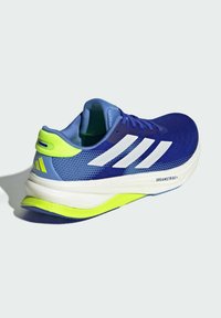 Blue athletic shoe with white stripes, mesh upper, and a textured sole. Features a green accent on the heel and "DREAMSTRIKE" branding.