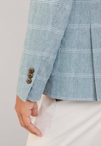 Blazer a quadri azzurro chiaro realizzato in un tessuto texture, con tre bottoni marroni ai polsi e uno spacco sul retro.