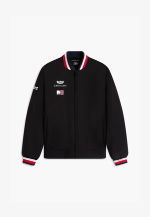 Czarna kurtka na suwak z czerwono-biało-granatowymi paskami na kołnierzu i mankietach, z logo Cadillac Formula 1 i Tommy Hilfiger na przodzie.