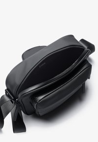 Borsa a tracolla nera in pelle con texture liscia, tasca frontale con zip e interno foderato in poliestere. Presenta una tracolla regolabile e un design minimale.