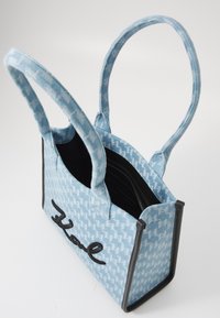 Vaaleansininen houndstooth-kuvioinen kassi mustilla yksityiskohdilla ja edessä brodeerattu "Kale", jossa on kaksi kahvaa ja avoin yläosa, jossa on sisempi vetoketjullinen tasku.