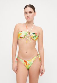 Biquíni de dois peças com um vibrante padrão floral em verde, laranja e amarelo. O top é sem alças e apresenta um detalhe de laço; as partes inferiores têm laços laterais.
