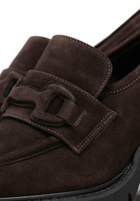 Mocassins en daim marron avec une sangle texturée et une boucle décorative, des coutures contrastées et une semelle épaisse.
