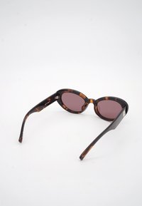 Οβάλ γυαλιά ηλίου με ταρταρούγα πλαίσιο και σκουρόχρωμους φακούς, τοποθετημένα σε λευκή επιφάνεια, με γωνία που δείχνει μπροστινή και πλευρικά τα μπράτσα.