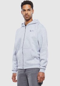 Gray zip-up hoodie with a hood, front pockets, and an embroidered logo. Made from soft fabric with a slightly textured finish.