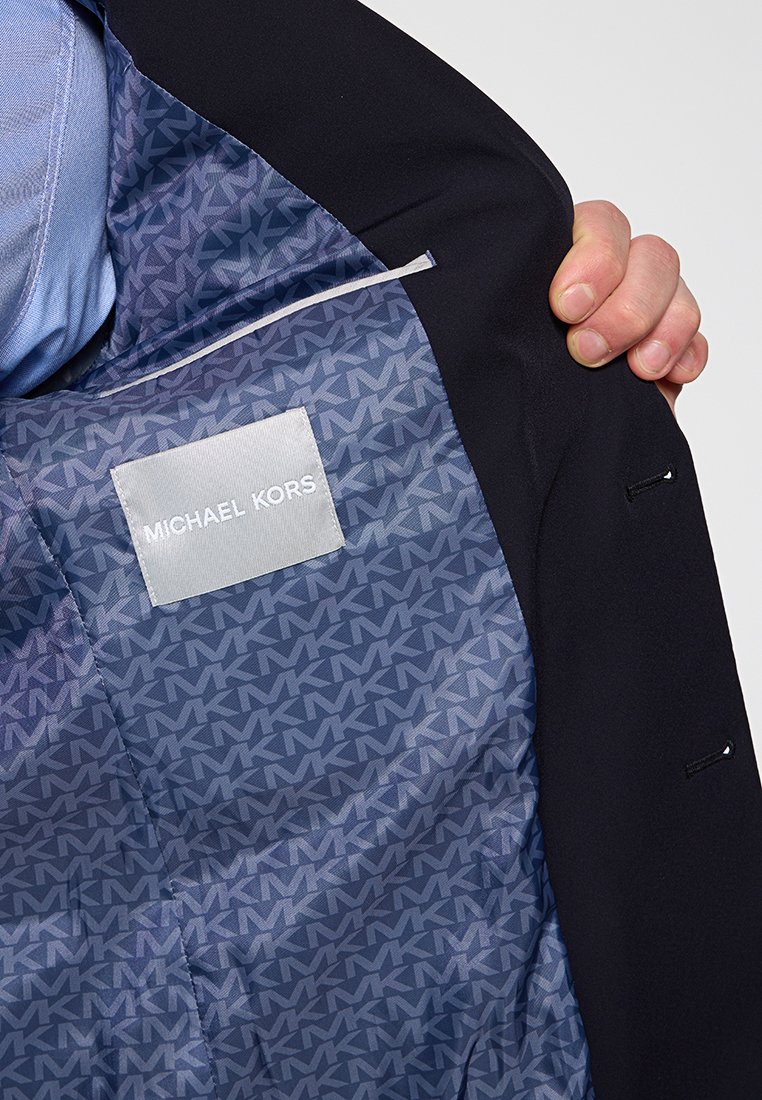Schwarze Blazer-Innenseite mit blauer Fütterung, die ein gemustertes "M"-Logo und ein gesticktes Etikett mit der Aufschrift "MICHAEL KORS" zeigt.