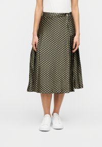 Μαύρη φούστα με σχέδιο γεωμετρικών μοτίβων, με υψηλή μέση και αέρινη σιλουέτα, συνδυασμένη με λευκά αθλητικά παπούτσια.