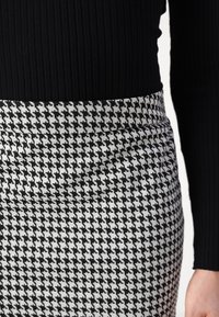 Högmidjad pennkjol i svart och vitt houndstooth-mönster, tillverkad av strukturerad tyg med en slät midjeresår.