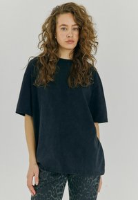 Černé oversize tričko s krátkými rukávy, které m�á jemnou texturu. V kombinaci s tmavými kalhotami s vzorem v odstínech šedé a černé.