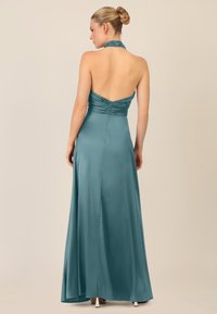Abito in satin turchese con scollatura a halter, corpetto arricciato e gonna fluente. Presenta una chiusura con cerniera sul retro e una leggera lucentezza.
