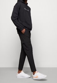 Svart huvtröja med text, tillsammans med svarta cargobyxor med fickor. Vita sneakers med orange detaljer fulländar outfiten.