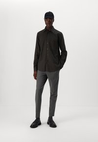Black and gray striped button-up shirt, gray tailored trousers, black cap, black shoes with chunky soles. Simple, modern design.