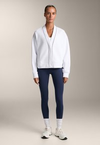 Bela oversize dukserica s crnim detaljima, uparena s mornarskim tajicama i bijelim tenisicama. Teksturirana tkanina i opušteni kroj.