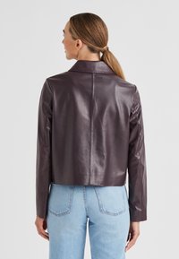 Geschnittene burgunderfarbene Lederjacke mit einem gepflegten Kragen, glatter Textur und taillierter Passform, kombiniert mit hellblauen Hochbundjeans.