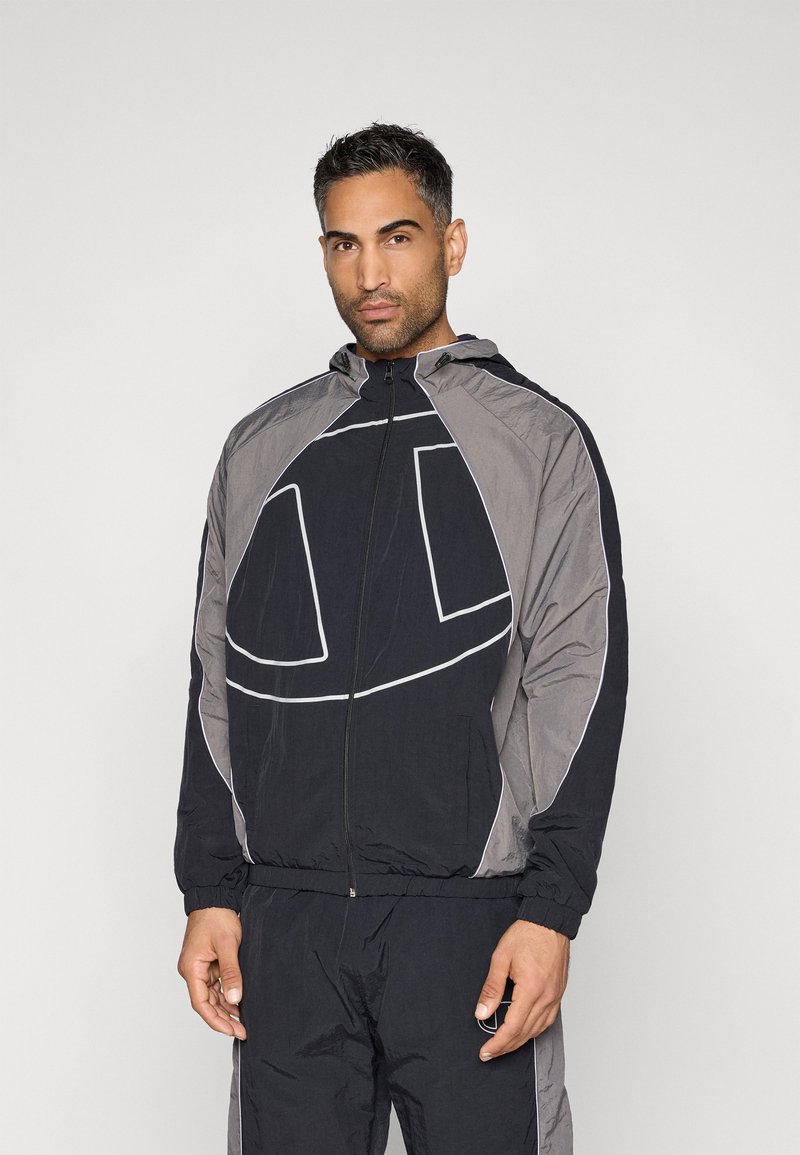 Chaqueta cortavientos negra y gris con capucha, que presenta un gran diseño gráfico, puños elásticos y cierre frontal con cremallera.