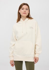 Kaptur spodnie w kolorze kremowym, z przednią kieszenią, elastycznymi mankietami oraz nadrukowanym wzorem gwiazdy z napisem "Bądź swoją własną gwiazdą". Miękka tekstura.