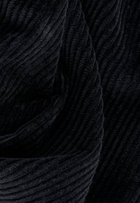 Zwarte corduroy stof met een geribbelde textuur, voorzien van een zachte pool en opvallende verticale ribbels. Soepel en dik materiaal.