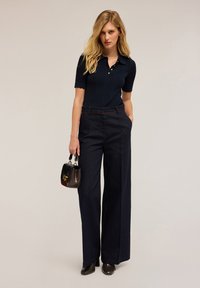 Polo a coste blu navy con maniche corte, abbinato a pantaloni in denim a gamba larga a vita alta. Gli accessori includono una borsa scura con una chiusura dorata.