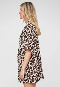 Abito camicia con stampa leopardata, caratterizzato da maniche corte, vestibilità comoda e tessuto leggero. I colori includono beige, nero e marrone.