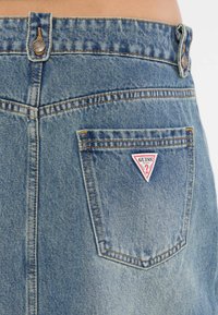 Spijkerrok in lichtblauw met een hoge taille, voorzien van een driehoekige rode en witte logo-patch op de achterzak en subtiele stikdetails.