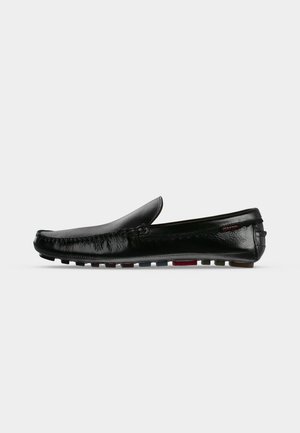 Mocassin en cuir noir sans lacets avec un bout arrondi et une semelle en caoutchouc multicolore sur un fond gris clair uni.
