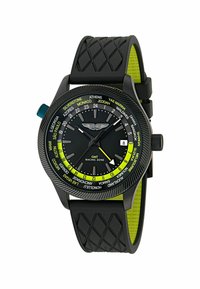 Reloj negro con correa de goma texturizada, acentos verdes y una esfera que incluye nombres de ciudades, números y una ventana de fecha a las 3 en punto.