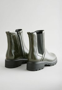 Las botas Chelsea verdes de cuero presentan paneles laterales elásticos, un zipper trasero y una suela de goma negra gruesa con un diseño texturizado.