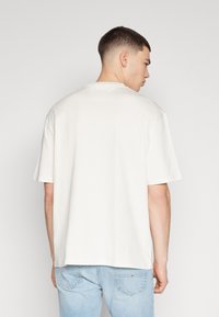 Camiseta de manga corta color crema con un corte relajado, con cuello redondo y textura de algodón suave, combinada con jeans de color azul claro.