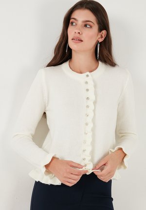 White cardigan with a ruffled edge and round neck; features buttons down the front and long sleeves with ruffled cuffs. Soft texture.