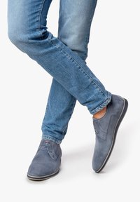 Scarpe oxford in suede grigio con lacci e cuciture tonali, abbinate a jeans blu chiaro a gamba dritta, che mettono in mostra un look casual.