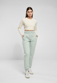 Ljust beige croppad långärmad topp i kombination med mintgröna sweatpants med elastisk midja och dragsko, samt fickor. Vita sneakers.
