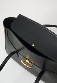 Sac à main en cuir noir avec une texture lisse, doté d'un fermoir ovale en or et d'une ouverture avec rabat. Comprend deux anses noires pour le transport.